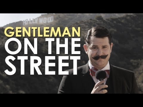 A gentleman in a suit is holding a microphone in front of a Hollywood sign.
