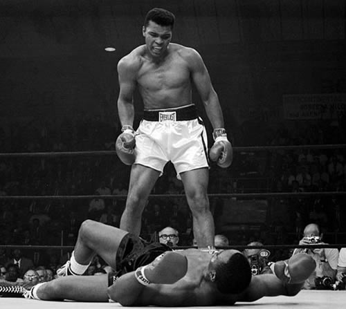 Muhammad Ali stands and Sonny Liston Muhammad Ali stands over Sonny Liston in boxing ring.