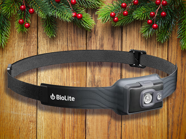 A black BioLite headlamp with an adjustable strap is displayed against a wooden background decorated with pine branches and red berries—perfect as one of the best stocking stuffers for men this season.