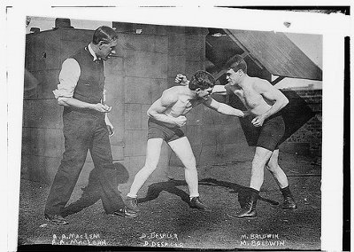An old photo showcasing the basics of boxing with three men in boxing attire.
