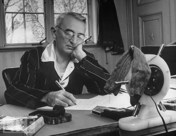 An elderly man in a suit writes at his desk, head resting on his hand, reflecting perhaps on the "Damned Fool Things I Have Done." Nearby, a sock hangs on a circular frame.