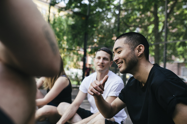 A group of people sitting on the ground in a park, engaging in an episode of their podcast.