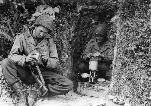 Two WWII soldiers sitting in a cave, enjoying a cup of coffee.