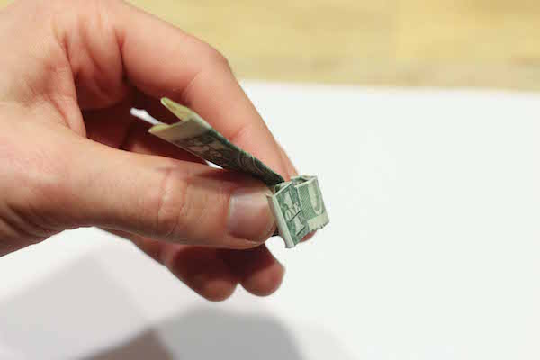 Folding vertical section of dollar bill down by hand.&nbsp;&nbsp;