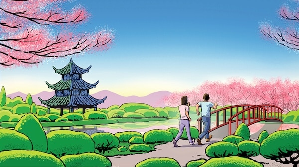Two people practicing 3X3 Interval Walking towards a traditional Asian pagoda, crossing a red bridge in a lush park with blooming pink trees.