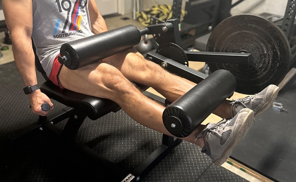 A person using a leg extensions machine at a gym, focusing on the lower body exercise with visible effort.