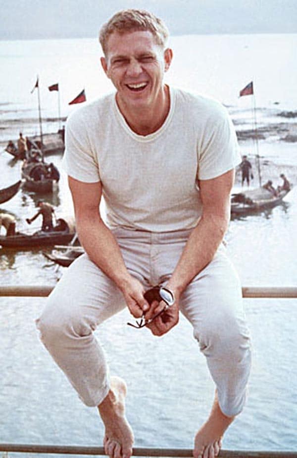 Steve mcqueen sitting on ocean railing.