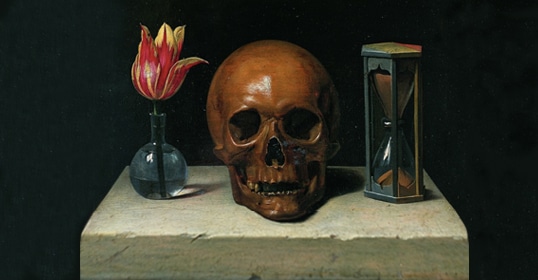 A red and yellow tulip in a glass vase, a human skull, and an hourglass are arranged on a stone table against a dark background, evoking the idea to make friends with death as we strive to live a better life.