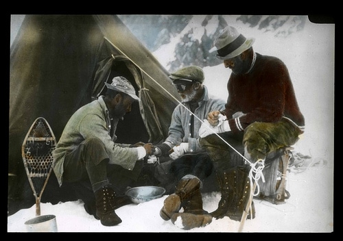Three men sitting around a tent in the snow, engaged in a profound manvotional discussion.