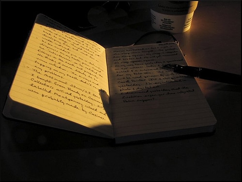 A moleskine notebook on a table with a cup of coffee next to it.