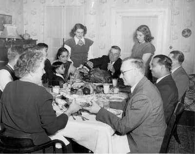 A group of people sitting around a table, enjoying Thanksgiving dinner with cornbread stuffing.