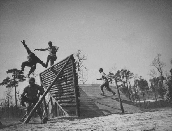 Vintage soldiers jumping over obstacle at bootcamp.