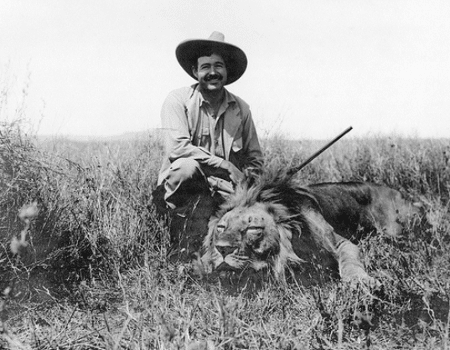 A man on an African Safari adventure, kneeling in the grass next to a majestic lion.
