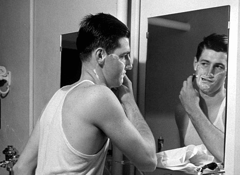 A wet shaver carefully grooming in front of a mirror.