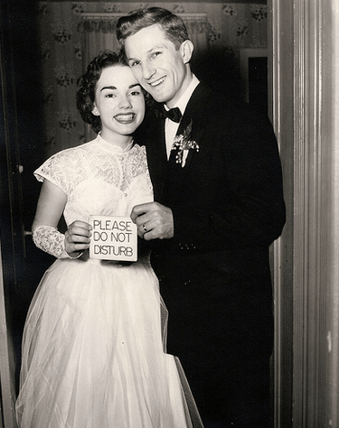 Vintage couple on wedding day holding "please do not disturb" card.